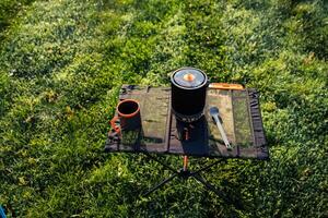 A convenient and portable camping cooking setup featuring pot and utensils resting on lush green grass photo