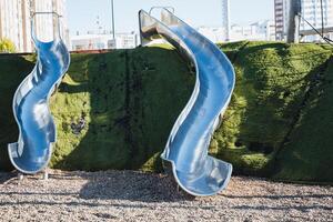 A lively playground features two shiny blue stainless steel slides, offering fun for kids and thoughtful urban design, ideal for leisure activities and family gatherings photo