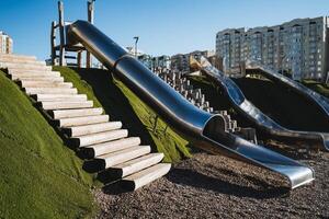 A playground features a shiny stainless steel slide, complemented by a sturdy set of stairs that lead up to the top, making it an exciting attraction for children to enjoy their playtime photo
