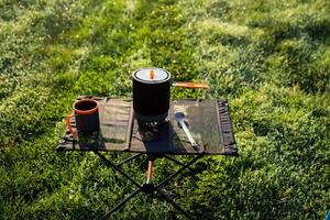 A table with a pot , cup and spoon on it in the grass photo