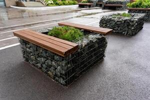 A wooden bench is positioned comfortably and securely atop a stone planter, creating a delightful combination of natural materials and practical urban seating for people to enjoy photo