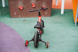 A striking red and black bicycle featuring training wheels is parked in a lively playground, inviting children to enjoy the fun and excitement that this vibrant setting offers photo