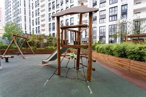 There is a wooden playground featuring a slide and swings situated right in front of a building, providing a fun recreational space for children and families to enjoy together photo