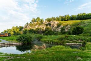 A mesmerizing view is presented as a beautiful train passes peacefully by a tranquil lake surrounded by lush greenery under a captivating sky with fluffy clouds overhead photo