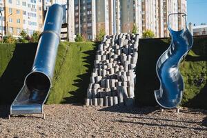 In a lively park, there are two shiny metal slides positioned right next to each other, inviting children and families to come and enjoy them on a sunny day of fun and play photo