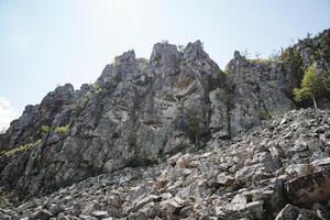 The mountain is adorned with rocks and trees, creating a breathtaking natural scenery under the vast sky. Its a captivating view of cliffs and hills that mesmerizes the eye photo
