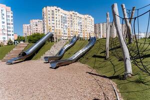 The playground provides a range of slides set against a cityscape backdrop in an urban environment with asphalt and a condominium facade, creating a distinctive leisure experience photo