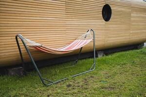 In a serene outdoor setting, a lively hammock on a metal frame stands next to wooden siding, offering a tranquil escape in a lush grassy yard for relaxation and leisure photo