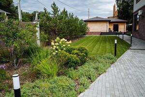 A charming brick walkway gracefully leads to a beautiful house that is surrounded by a lush and vibrant green lawn, adding to the overall picturesque scenery of the environment photo