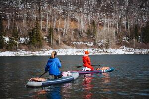 Women float on a SUP board on the river against the background of mountains, rowers with a paddle on a board, tourists sail on the lake, outdoor recreation. photo