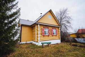 Discover the charming yellow log house adorned with red windows, beautifully surrounded by nature, creating an idyllic escape for relaxation photo