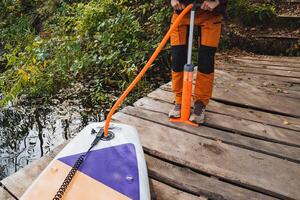 Man inflating a SUP board with air using a hand pump, orange hose, hose attachment to a board. photo