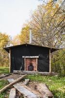 In the center of a lush forest, there stands a charming small hut complete with a chimney, surrounded by towering trees and vibrant greenery, making it a picturesque natural scene photo
