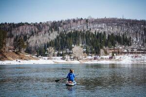Woman floating on a stand-up paddle board on the river against the background of mountains, beautiful landscape, view from the water, man sitting on a board with a paddle. photo