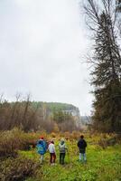 A diverse group of individuals is standing together in a beautiful, grassy field under the open sky, enjoying the natural landscape that surrounds them, which includes trees and clouds photo
