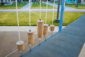 In a vibrant park, you can find a row of beautifully crafted wooden cylinders that are suspended by sturdy ropes, creating a playful and inviting atmosphere for visitors to enjoy photo