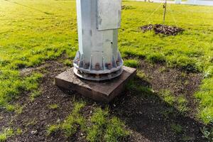 A sturdy metal pole is firmly positioned on a solid concrete base, which is surrounded by lush green grass in the nearby area, creating a striking contrast between materials photo