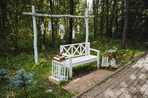 A beautiful white bench is sitting gracefully in the very middle of a serene forest, surrounded by lush greenery and tall trees, creating a peaceful and inviting atmosphere photo
