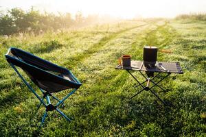 A peaceful and serene outdoor camping setup featuring a comfortable chair and table amidst morning mist photo