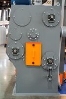 A large, robust industrial machine, which is characterized by its gray and orange coloring, is presently positioned on a smooth, durable concrete floor within a workshop or factory setting photo
