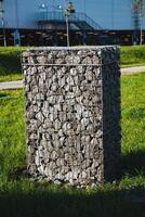 A large and imposing rock wall is positioned prominently in the lush green grass that lies right in front of a building, creating a striking visual contrast in the landscape photo