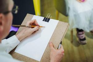 Man jotting notes on clipboard with pencil and eyewear on table photo