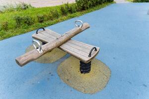 A wooden seesaw is currently placed on a blue surface within a park photo