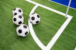 There are three soccer balls that are resting on the corner of a grassy soccer field, waiting to be used in an exciting game of soccer, also known as football in many countries photo