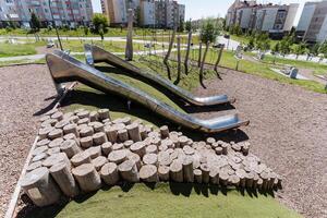 The park features a distinctive play area combining a metal slide and wooden logs, creating a harmonious urban design fusion of metal, wood, and nature. Its an artistic blend of elements photo