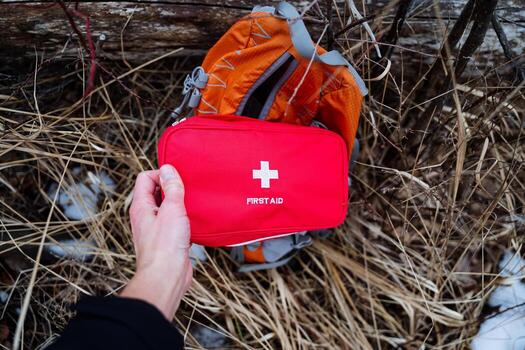 un persona es en pie y participación un brillante rojo primero ayuda equipo Derecha en frente de un naranja mochila, cuales agrega a el en general escenas color y contexto mientras exhibiendo necesario artículos foto