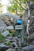 A determined man, passionate about adventure, climbs a steep hill with a sturdy backpack, pausing to enjoy the breathtaking scenery and soothing sounds of nature around him photo