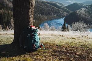 Beautiful mountain landscape, backpack standing by a tree, first aid kit lying on backpack, outdoor recreation, camping in the forest. photo