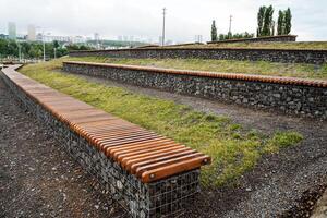 A wooden bench by a stone wall offers a peaceful spot to relax and enjoy the serene view of the landscape. Lush greenery and clear skies complete the tranquil scene, perfect for serenity photo