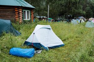 A blue tent stands on green grass next to a bag, offering shelter for relaxation outdoors, resembling a temporary dwelling in the open field with a calming natural landscape around photo