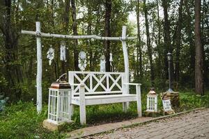 In the heart of a beautiful, serene forest, there is a white wooden bench that is positioned gracefully amidst the surrounding trees and greenery, inviting visitors to rest and enjoy nature photo