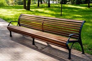 A long, sturdy wooden bench is situated in a beautiful park, surrounded by lush green trees in the background, creating a peaceful outdoor setting for relaxation and enjoyment photo