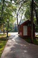 A charming and quaint small wooden shed is beautifully situated right beside a winding path that runs through a picturesque park, surrounded by lush greenery and scenic nature all around it photo