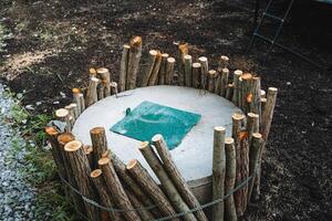 Nestled in a peaceful natural environment, a large concrete cylinder is surrounded by wooden poles and a vibrant green tarp, forming a unique and creatively designed structure photo