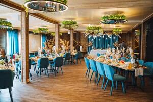 The spacious dining room features numerous tables and elegant chairs meticulously arranged for a joyful wedding reception, creating a warm and inviting atmosphere for the guests photo