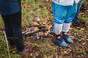 A person is standing closely beside a child in front of a blazing fire, which adds a cozy warmth and illumination to the memorable moment they are experiencing together outdoors photo