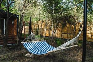 A hammock with calming blue and white stripes gently sways in a peaceful forest, offering a serene spot to relax in natures beauty and find tranquility amid a lush green environment photo