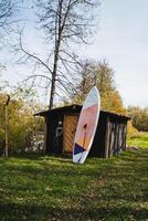 In a serene natural landscape, a surfboard is casually leaning against a rustic wooden shed, surrounded by lush green grass, capturing the essence of a laidback outdoor atmosphere photo