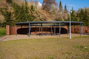 A designated covered area located within a park, featuring several trees in the background that enhance the natural beauty of the surroundings and provide a tranquil environment photo