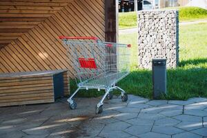An empty shopping cart is currently parked on the sidewalk right in front of a wooden bench, creating a scene that captures the essence of everyday life in an urban environment photo
