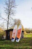 Two vibrant surfboards are leaning casually against a wooden shed, surrounded by lush green grass, creating a relaxed atmosphere perfect for a day of beachside fun and enjoyment photo