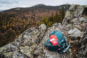Camping equipment lies in the mountains against the background of the autumn forest, mountain hiking, first aid kit in backpack, mountain tourist equipment. photo