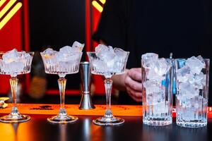 Cocktail preparation with ice in elegant glasses at a bar during the evening photo