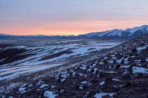 Soft pink light glides over the snow-capped peaks of the mountain photo