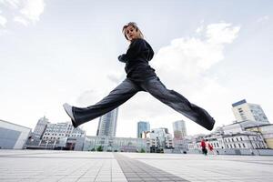 Young woman jumping across an urban square with buildings in the background photo