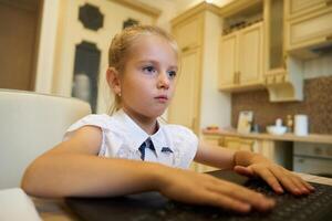 Young girl concentrating while typing on a laptop in a cozy kitchen setting photo